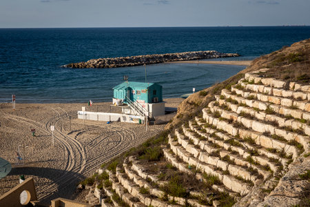 An empty urban beach in Ashkelon, Israel, on October 2, 2024, showcasing wave breakers, wooden shelters for sun protection, and a lifeguard cabin.の写真素材