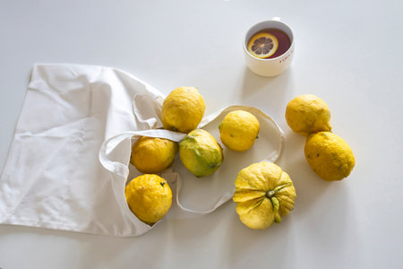 Fresh yellow lemons in a white cloth bag on a white table indoors, with a white mug in the background. Copyspace.の写真素材
