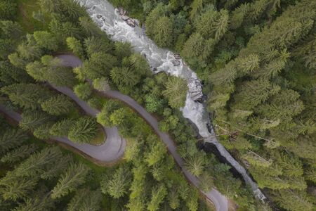 photo taken with a drone flying over an S shaped road in a conifer and an waterfall in a soft...