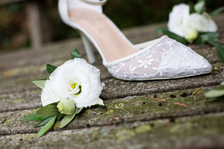 Detail of a single white wedding white shoe with embroidery and heel placed on top of old ruined wooden planks and surrounded by white flowers with olive leavesの写真素材