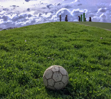 A white colored football lies at the bottom of a grassy slope in the play area on a warm sunny dayの写真素材