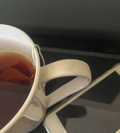 Partial view of black tea in a white mug next to a black screen mobile phoneの写真素材