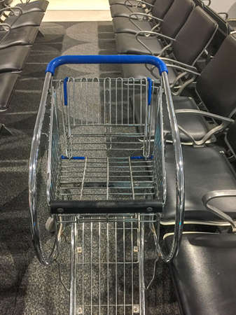 Metal shopping trolley in between a row of black leather chairsの写真素材