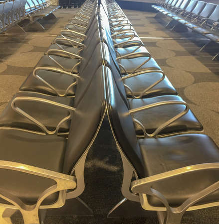 Two rowa of black leather chairs with metal hand rests lined up against each other back to back in a waiting areaの写真素材