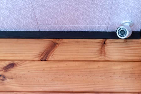 Home security camera installed in the corner of the white ceiling and timber wall