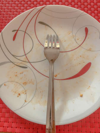 Overhead view of dirty ceramic plate with a silver fork lying face down on itの写真素材