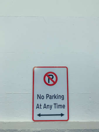A no parking at any time metal sign with a double headed horizontal arrow against a white brick wall backgroundの写真素材