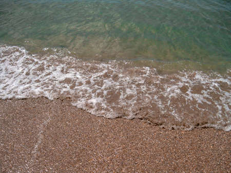 Overhead view of th edge of a foamy wave drifting onto the beach on a bright sunny dayの写真素材