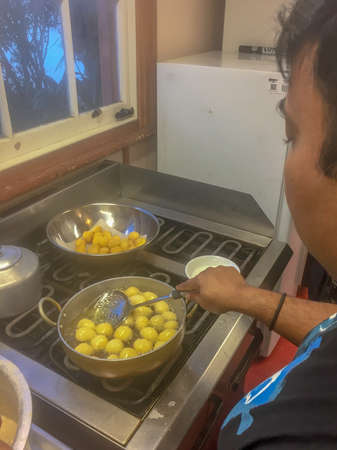 Saturday 30th June 2018, Auckland New Zealand - a man stands in front of a four burner electric stove top and deep fries an East Indian traditional snack made of balls of dough known as fugiyas or balloon bread.のeditorial素材