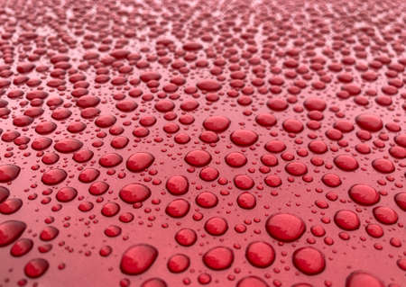 Raindrops close up abstract shot on a red car bonnet during the dayの写真素材