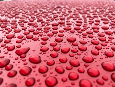 Raindrops close up abstract shot on a red car bonnet during the dayの写真素材
