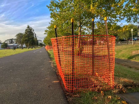 Orange plastic netting enclosing work areas along the paved pathway at the parkの写真素材