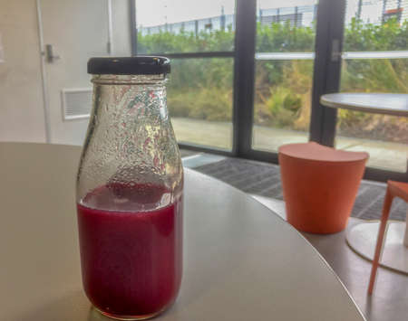 A glass bottle half full of red beetroot juice stands on a white lunch table in the office lunchroomの写真素材
