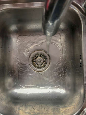 Overhead view of water flowing from a tap into a stainless steel sinkの写真素材