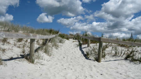Wooden fence entrance to white sandy beach on bright sunny dayの写真素材