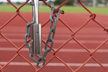 Silver lock and chain on metal fence securing red surface race trackの写真素材