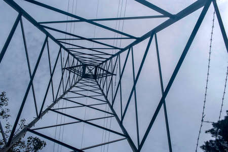 Upward view of an electrical pylon tower with cables running vertically under a dull blue skyの写真素材