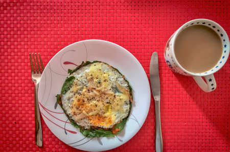 Overhead view of a mug of coffee and a plate of fried eggs on red table mat