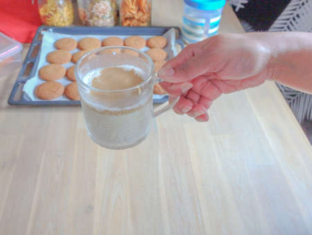 Female hand holding a glass of dalgona coffee with a tray of cookies in the backgroundの写真素材