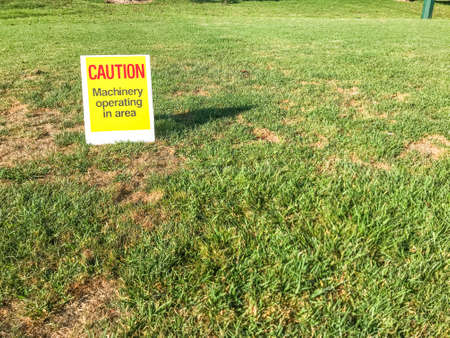 Caution sign indicating machinery operating in the area sitting on the grass of a public park during the day in the Auckland New Zealandの写真素材