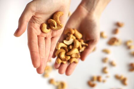 Nuts in the palms. Pour nuts from one palm to another. Cashew nuts sprinkled on a white background. Pour nuts in the palms.の写真素材