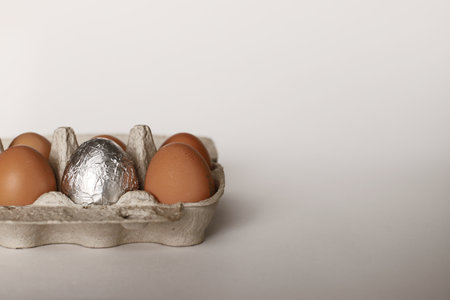 Chicken eggs in a container on a white background. One egg is silver. Easter eggs. Eggs in a...