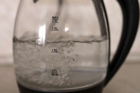 Transparent kettle in the kitchen. Water boils in a transparent teapot with a black handle. Boiling water in a kettle.の写真素材