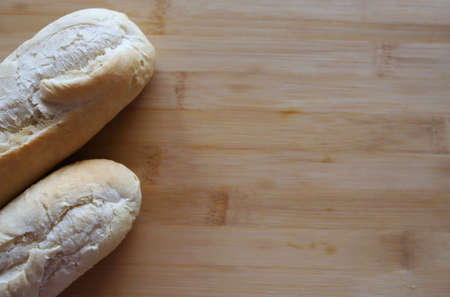 Two fresh baguettes on a wooden board with place for text. Beautiful wooden background with...