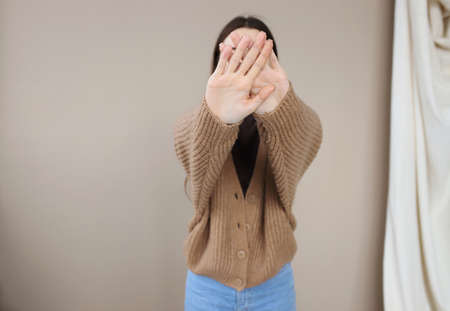 A young girl covers her face with outstretched arms forward. A girl in a brown knitted sweater covers her face with outstretched hands. Selectiv focusの写真素材