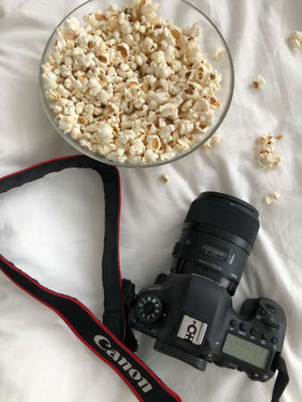 Black SLR camera Canon 6D Mark II on a white bed top view, with a cup of popcorn. vertical photo Russia Altai Territory, Barnaul 04.01.2021のeditorial素材