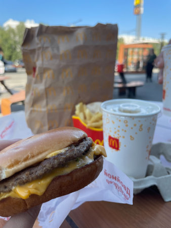 Cheeseburger in hand in the background a drink, fries from a McDonald's fast food restaurant in Barnaul. Russia, Barnaul, August 29, 2021. selectiv focusのeditorial素材