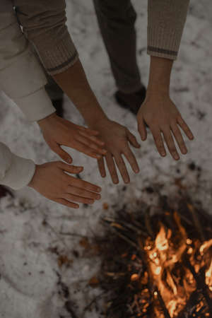 A guy and a girl yew their hands over a campfire in the winter. Close-up, Vertical photo.の写真素材