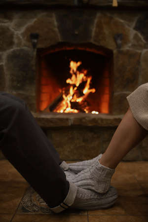 The feet of a man and a woman in warm socks next to the fireplace. Vertical, atmospheric photo. Selectiv focusの写真素材