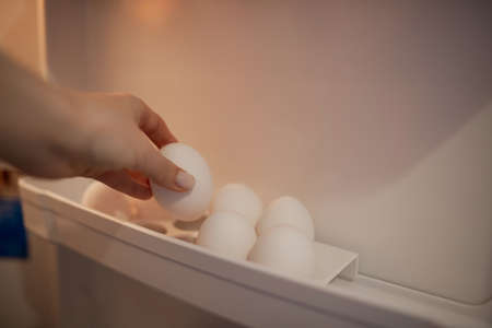 A girl puts white chicken eggs in the egg compartment in the refrigerator. A girl takes a chicken...