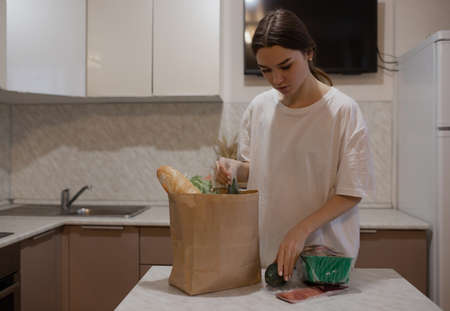 The girl lays out on the kitchen table products bought in the store. The woman takes the food delivered by courier from the bag. Selectiv focusの写真素材