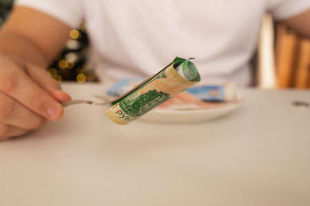 Russia, Barnaul, December 26, 2021: Money bill on a fork. A man eats money from a plate. Russian...