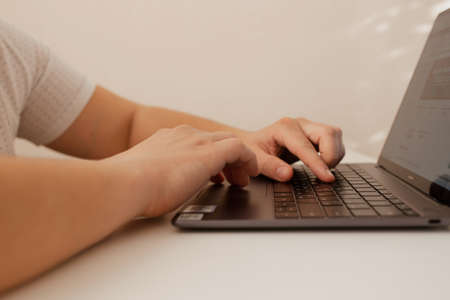 Russia, Barnaul, January 10, 2022: A man works at home on a laptop. A man prints text on a laptop. The man works at home. Distance work, distance learning. Close-up. Selectiv focusのeditorial素材