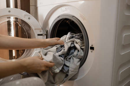 Russia, Barnaul, January 10, 2022: The girl loads the washing machine with dirty laundry. The girl...