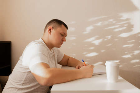 The man writes notes in the diary. A man writes notes at home. The guy writes notes in a notebook.