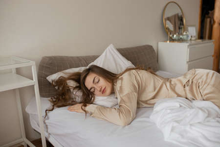 A young girl in stylish pajamas sleeps on a white bed. The girl sleeps in the hotel room.