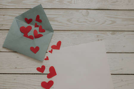 An open envelope with red hearts and a blank sheet of paper lies on a wooden background. Envelope with hearts, place for text.の写真素材