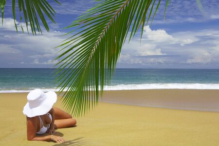 view of nice woman lounging on tropical beach in white panama and bikiniの写真素材