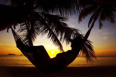 view of a woman lounging in hammock during sunsetの写真素材