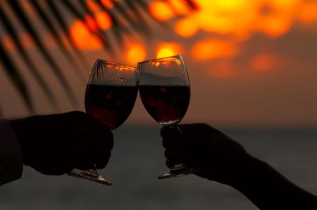 view of two humans hand with wineglasses during sunsetの写真素材