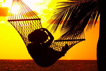 view of a woman lounging in hammock during sunsetの写真素材