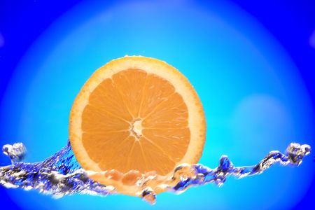 Close up view of sliced orange piece getting splashed with waterの写真素材