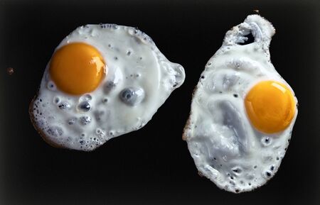 Close up view of two fried eggs on black backの写真素材