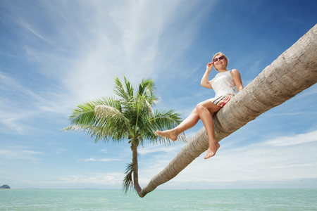 view of nice young lady sitting on palm  on tropical beach.の写真素材
