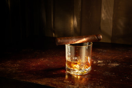 Closed up view of glass of whiskey with cigar on top on color back