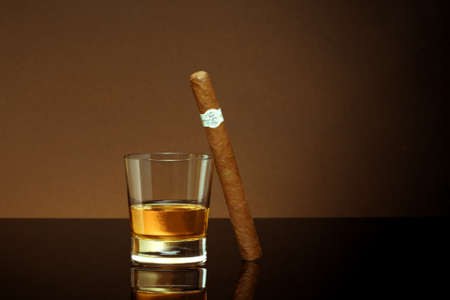 Closed up view of glass of whiskey with cigar on top on brown back